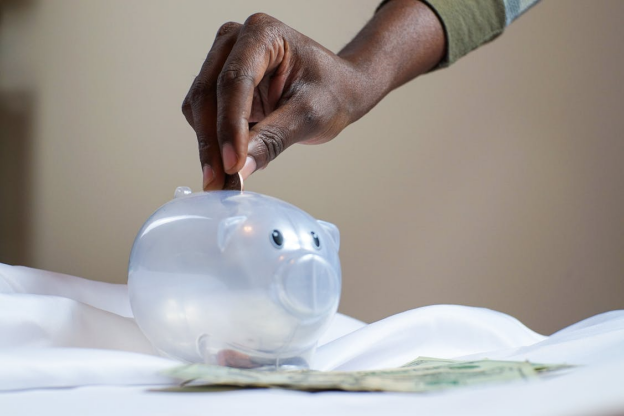 Close-up of a person putting a coin into a white piggy bank