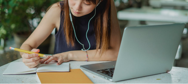 A focused student writing in a notebook with a laptop open, planning her academic and career goals.