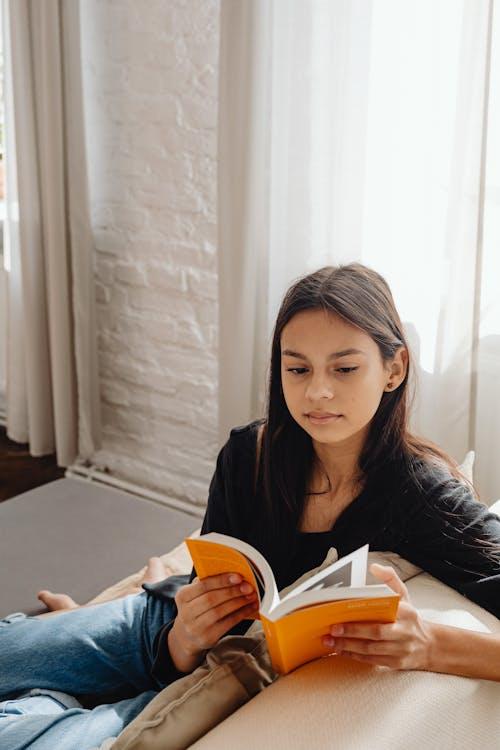 Young girl reading a book by the window on a bright morning