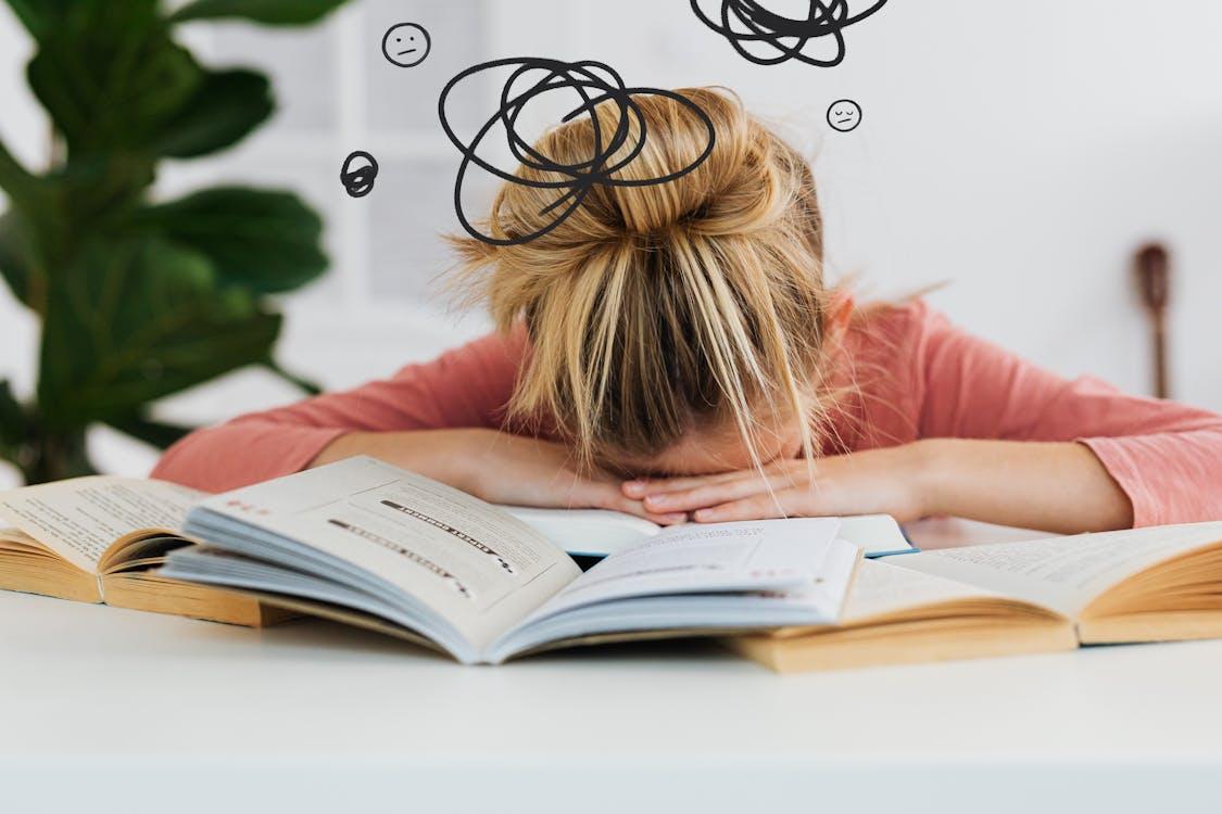 Tired student resting head on desk surrounded by a stack of books